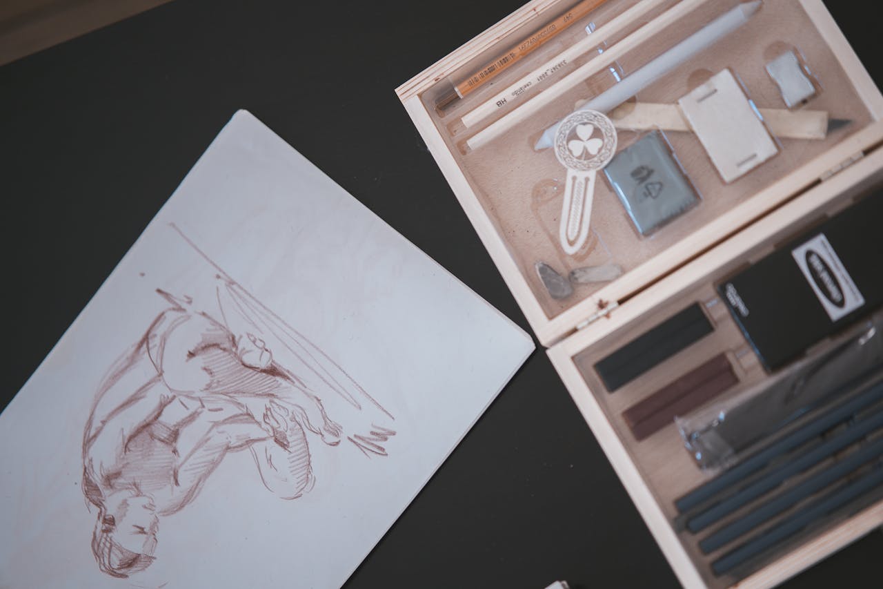 about-02 Overhead view of art supplies and sketch featuring human figure, perfect for creative projects.